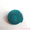 Broche artisanale en forme spirale turquoise et bronze scintillant avec léger ajourement entre les spirales encastrées.